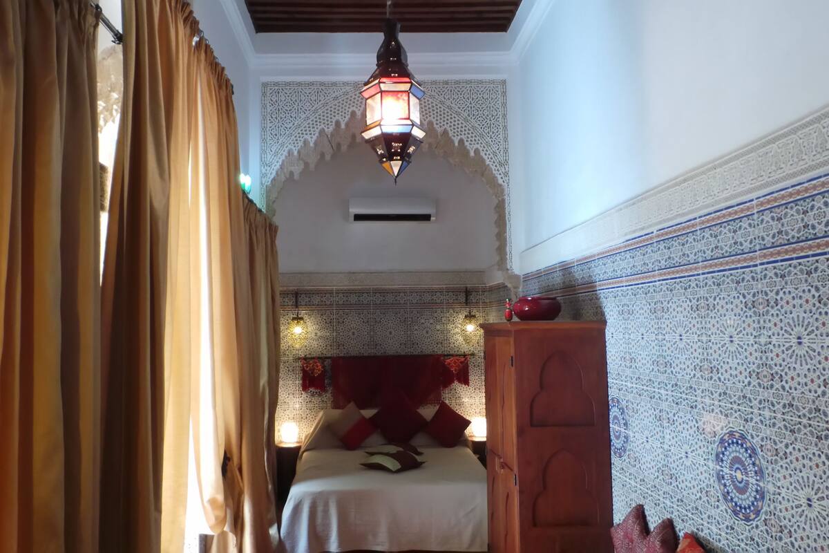 A room with a bed, a hanging lantern, and patterned walls.