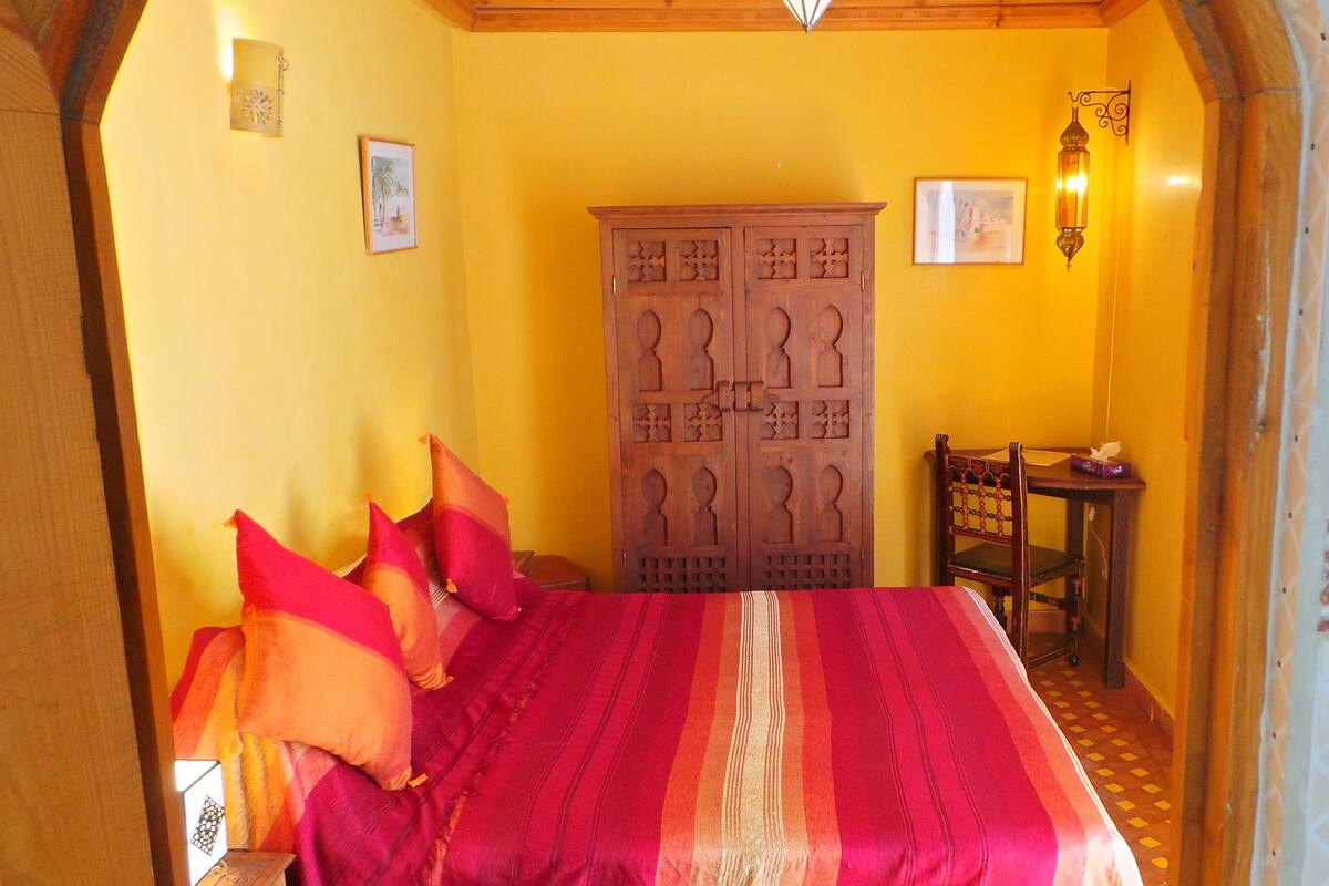 A room with a bed, a wooden cabinet, a table, and a chair.