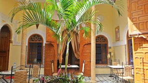 A courtyard with a palm tree, wooden doors, and tiled flooring. - Dar Zouhour (Rabat)