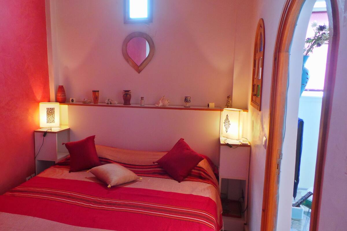 A bedroom with a bed, two bedside lamps, a shelf with decorative items, and a mirror.
