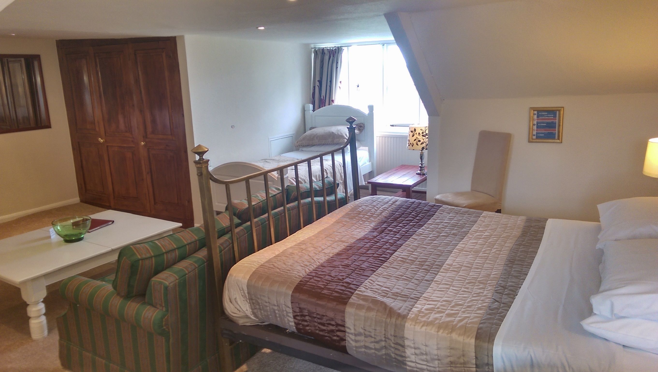Een slaapkamer met een bed, een tafeltje, een stoel, een raam met gordijnen en een deur.
