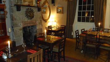 A dining area with a fireplace, wooden furniture, and a chandelier.
