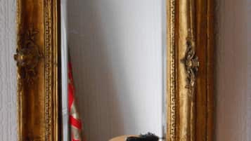A mirror with an ornate gold frame, reflecting a white wall and a red and white striped object.