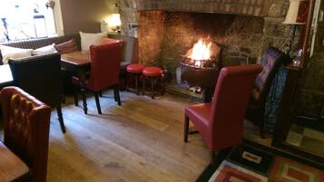 A cozy room with a stone fireplace, wooden flooring, and red upholstered chairs.