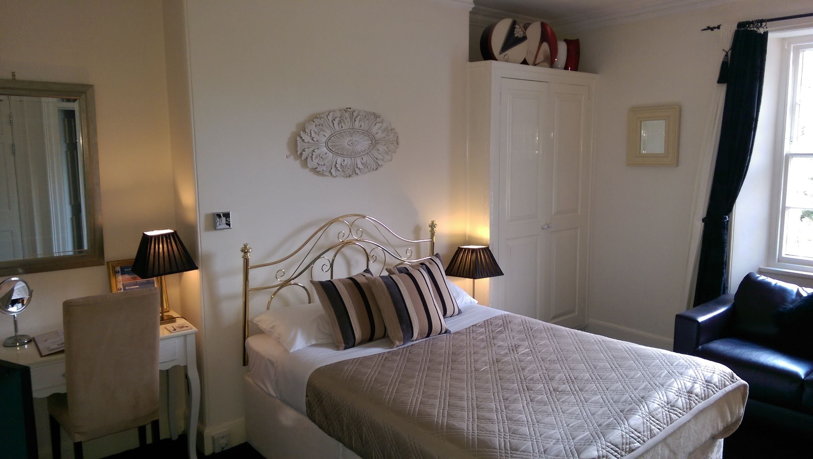 A neatly arranged bedroom with a bed, bedside lamps, a desk, and a chair.