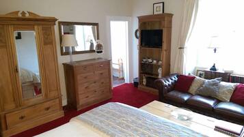 Un dormitorio con un armario de madera, una cama con cubrecama estampado, un sofá de cuero con cojines y un televisor sobre un mueble de madera.