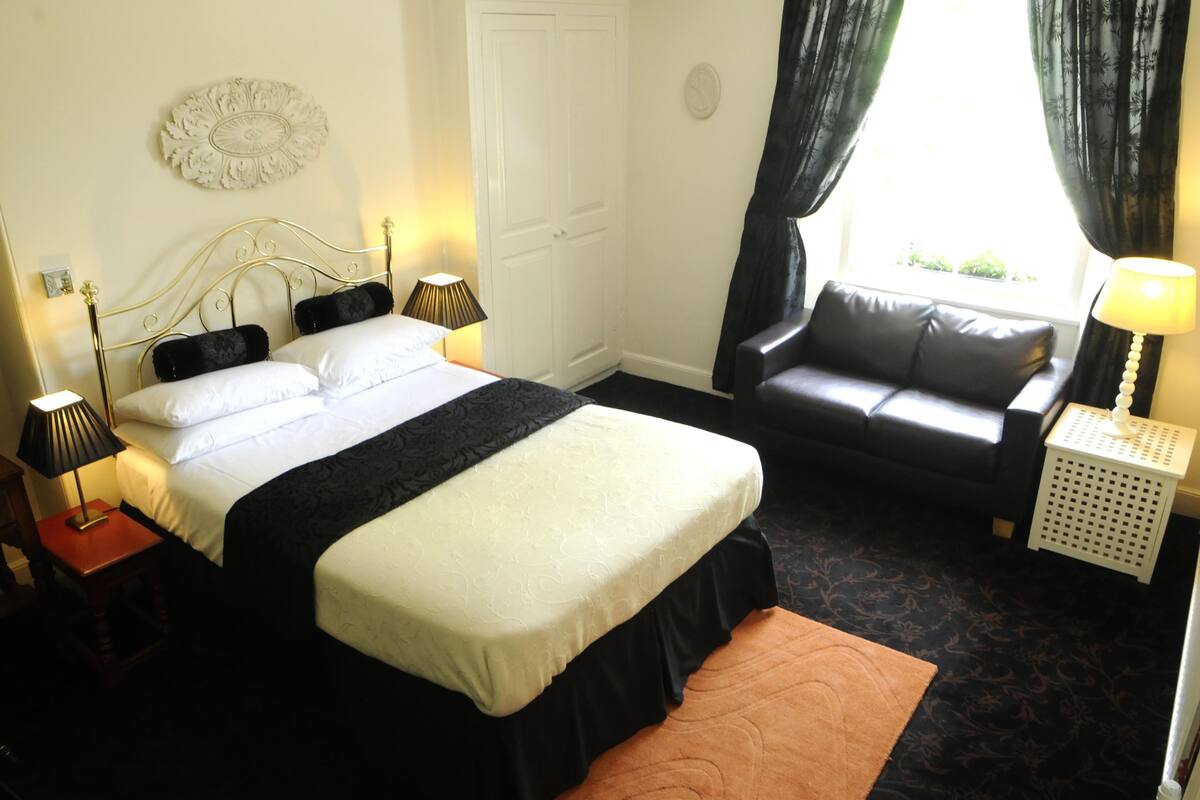 A neatly arranged bedroom with a bed, a sofa, and a small table with a lamp.