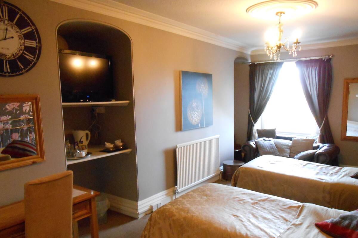 A hotel room with two beds, a television, a radiator, and a chandelier.