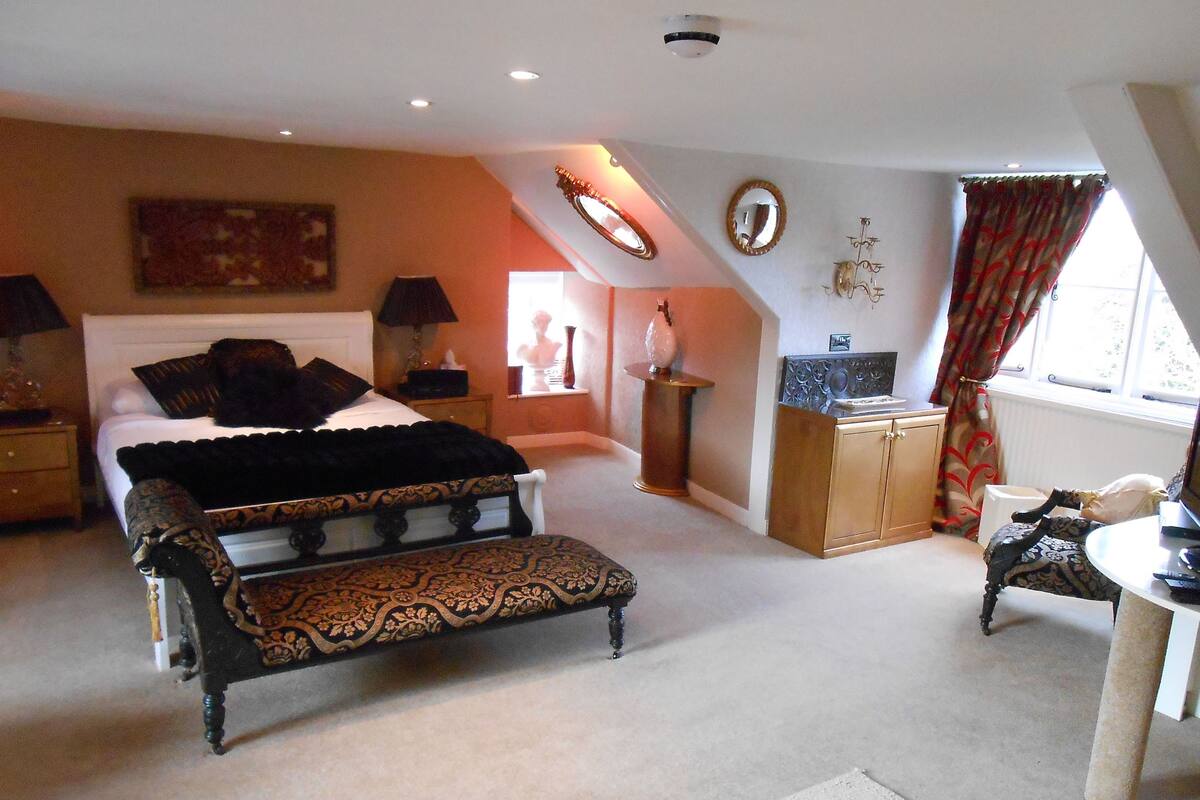 A bedroom with a large bed, a bench, a dresser, and a desk with a chair.