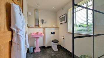 A bathroom with a wooden door, a pink sink, a toilet, and a window with blinds.