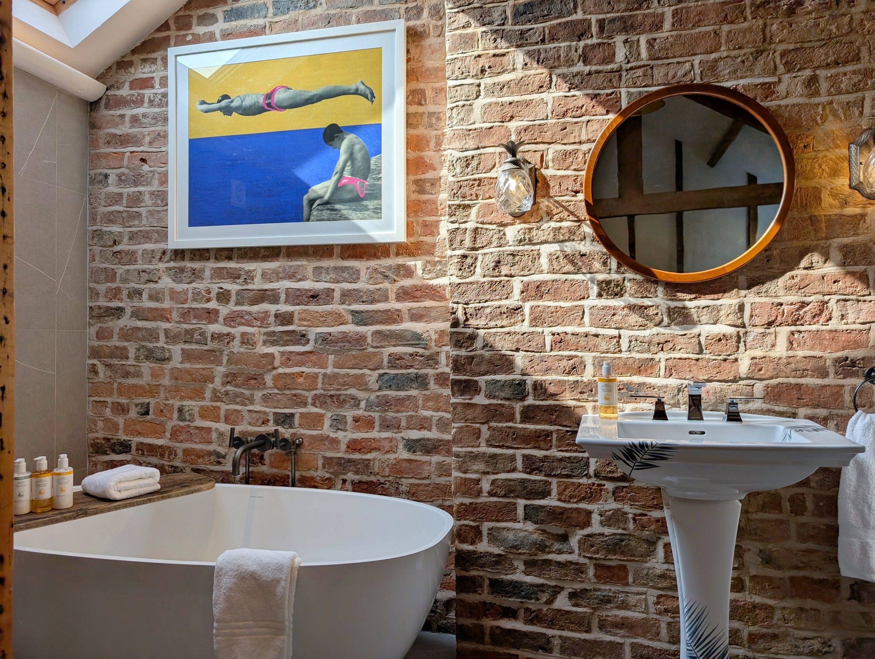 Un baño con una bañera grande, un lavabo, un espejo y una pared de ladrillo.