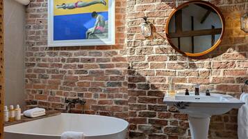 Un baño con una bañera grande, un lavabo, un espejo y una pared de ladrillo.