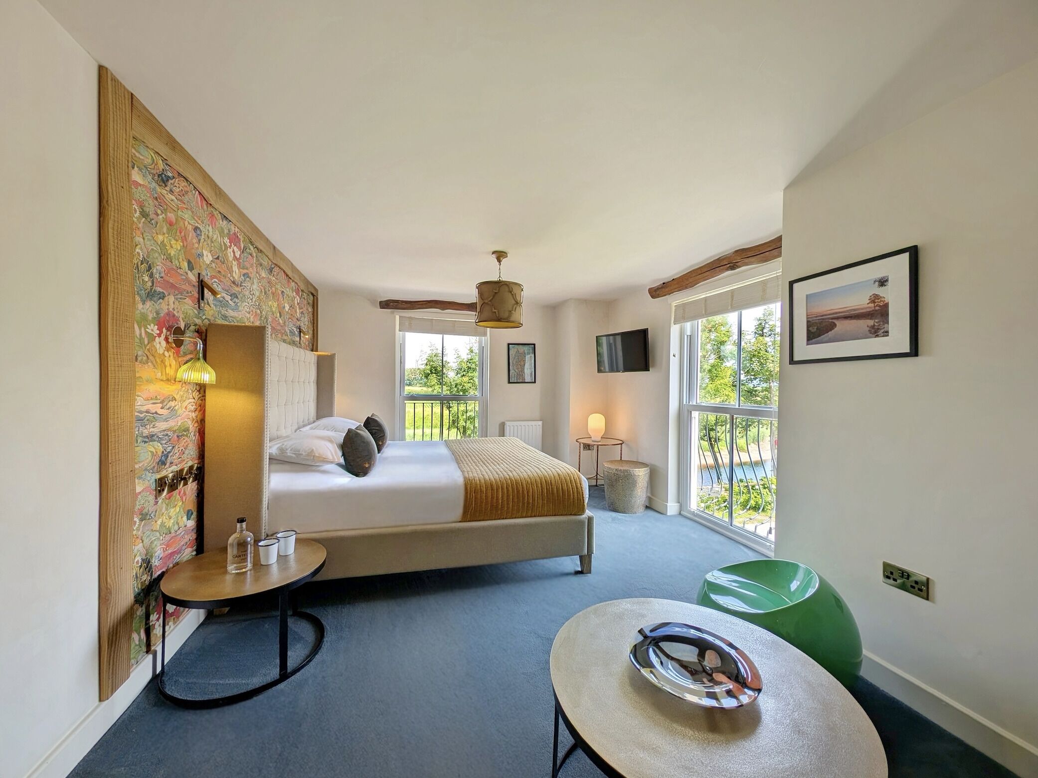 Une chambre avec un grand lit, une petite table, une chaise verte, un téléviseur et une fenêtre donnant sur des arbres.