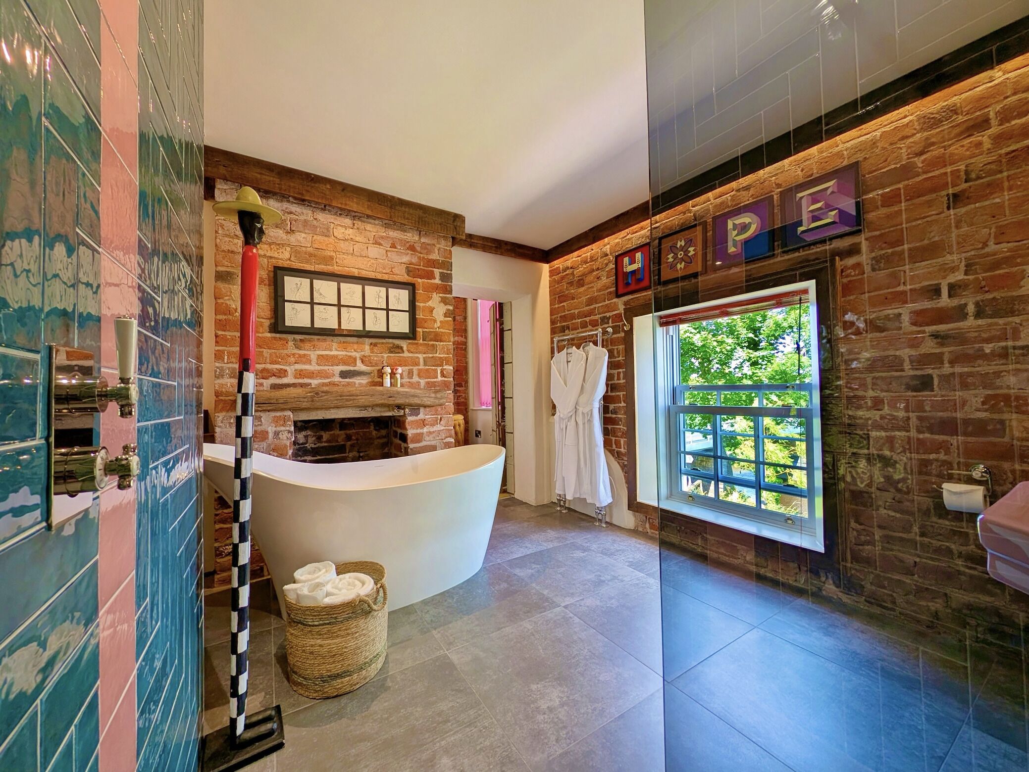 A modern bathroom with a freestanding bathtub, a brick wall, and a large window.