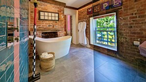 A modern bathroom with a freestanding bathtub, a brick wall, and a large window.
