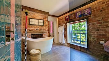 A modern bathroom with a freestanding bathtub, a brick wall, and a large window.