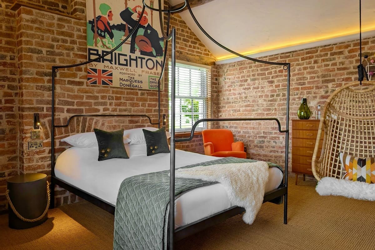 A room with a four-poster bed, a brick wall, a poster, and a wicker chair.