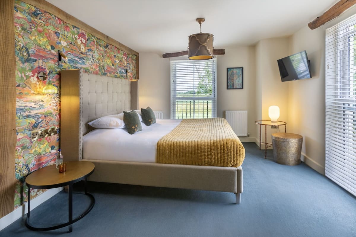 A bedroom with a bed, a wall-mounted TV, a window with blinds, and a decorative wall.