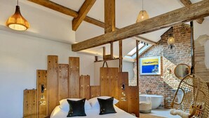 A bedroom with a wooden headboard, a bed with two black pillows, a hanging chair, and a brick wall with a painting. - The Cartford Inn (Preston)