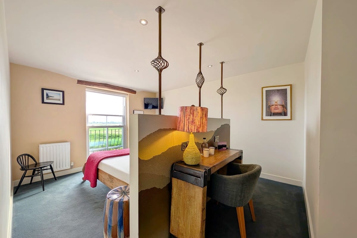 A bedroom with a bed, a desk, a chair, a radiator, a window, and a view of the outdoors.