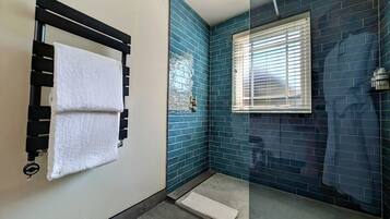 A bathroom with a glass shower enclosure, a towel rack with two towels, and a window with blinds.