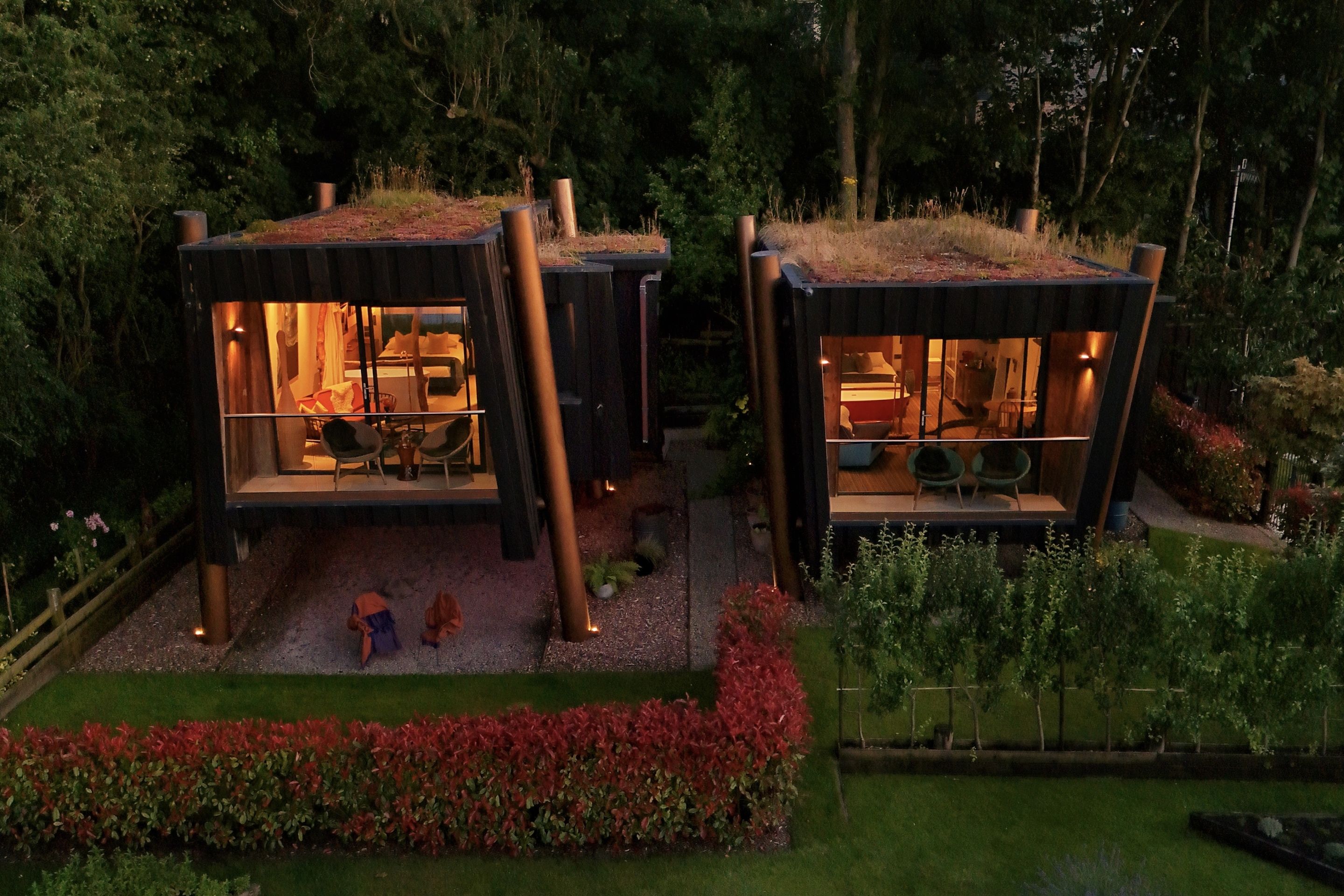 Two modern cabins with glass walls, a dining area, and a small outdoor space with red flowers.