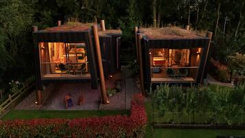 Two modern cabins with glass walls, a dining area, and a small outdoor space with red flowers.