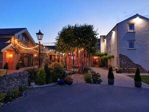 Une cour d’hôtel avec un mur en pierre, des plantes en pot et un chemin menant à l’entrée.
