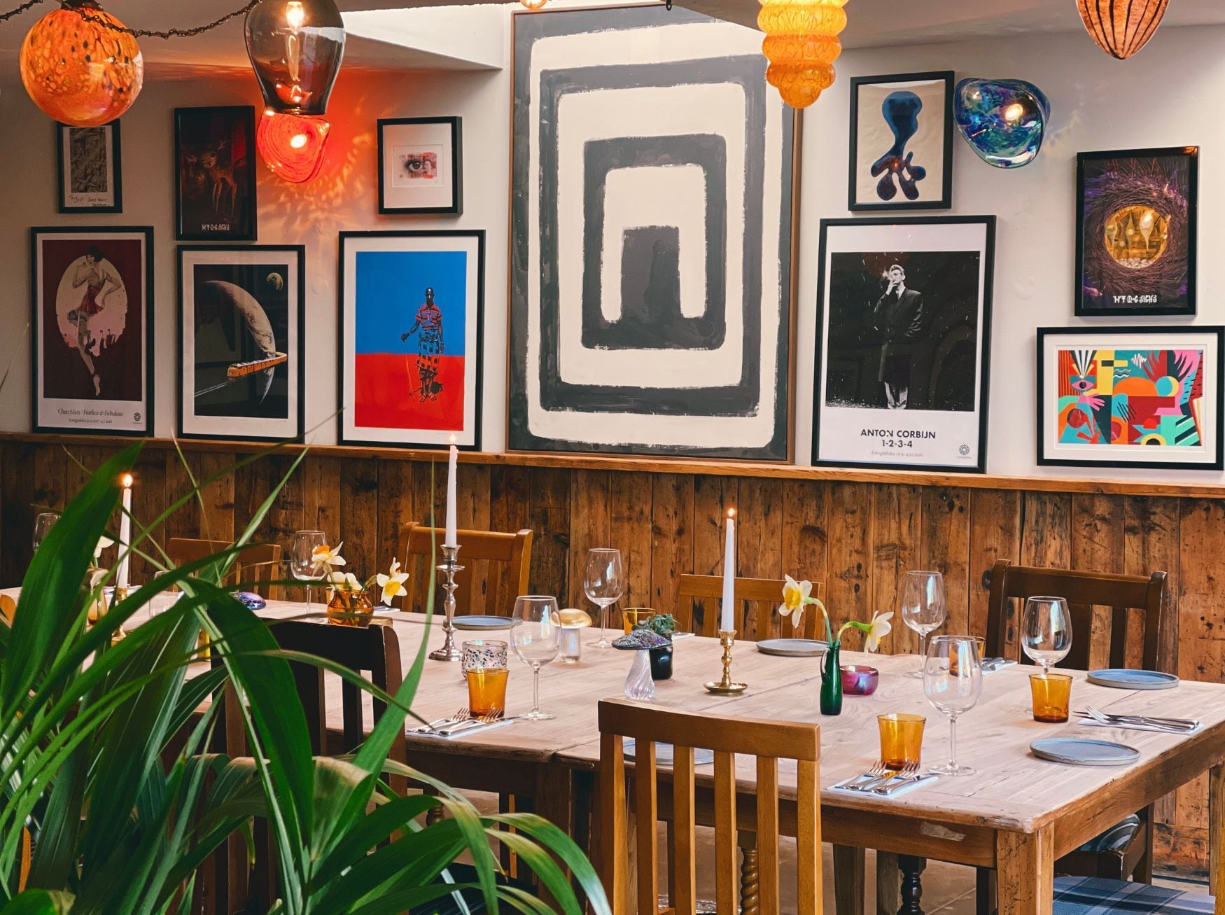 A dining area with a wooden table set for two, surrounded by framed artwork on the walls.