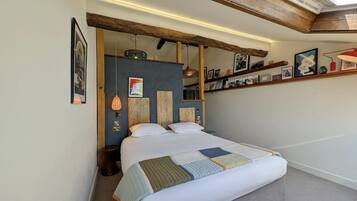 Un dormitorio con una cama grande, tragaluz, techo con vigas de madera y estante con cuadros enmarcados.