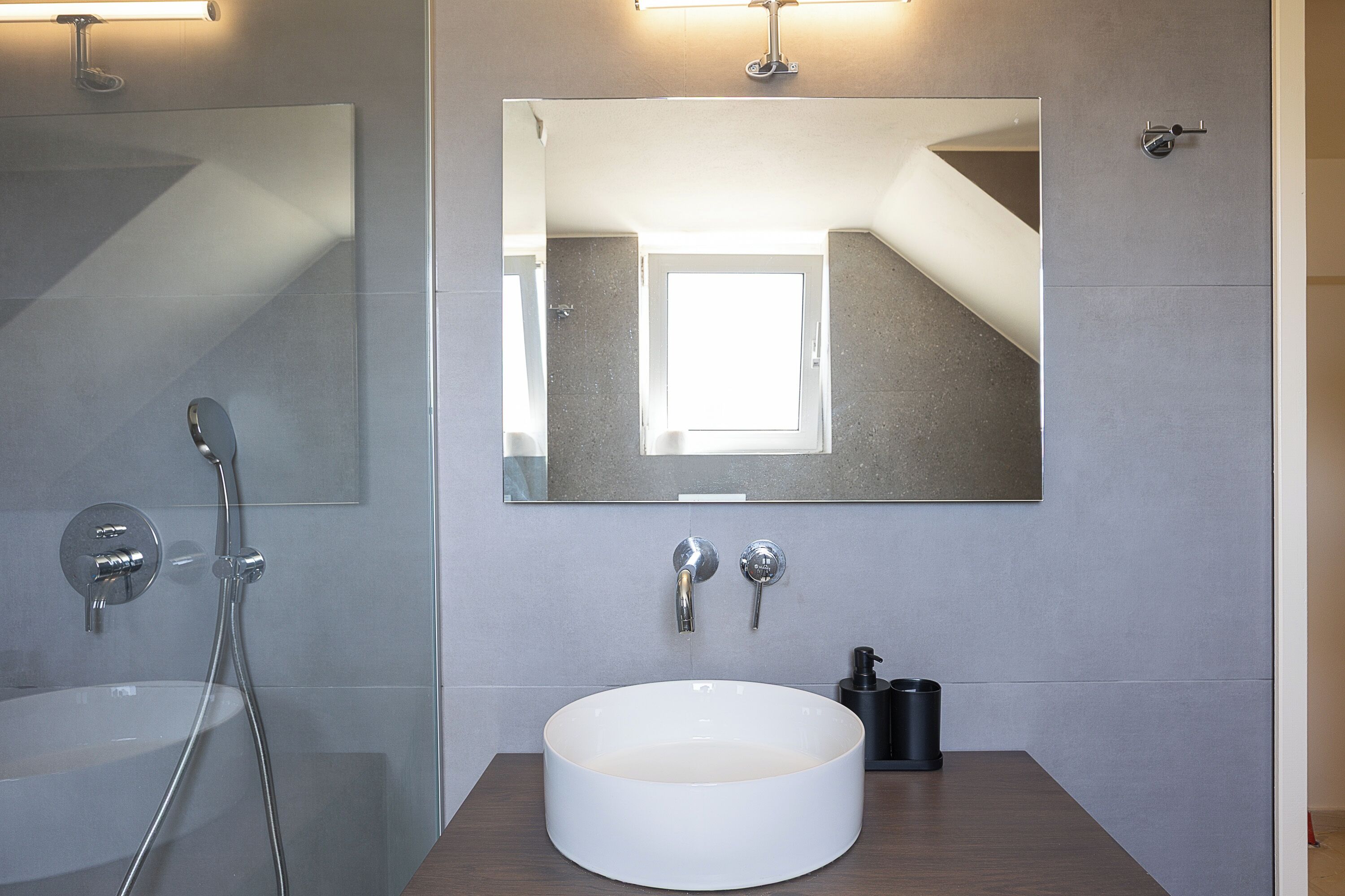 Een moderne badkamer met een grote spiegel, een rond wasbakje en een douche met een handdouche.