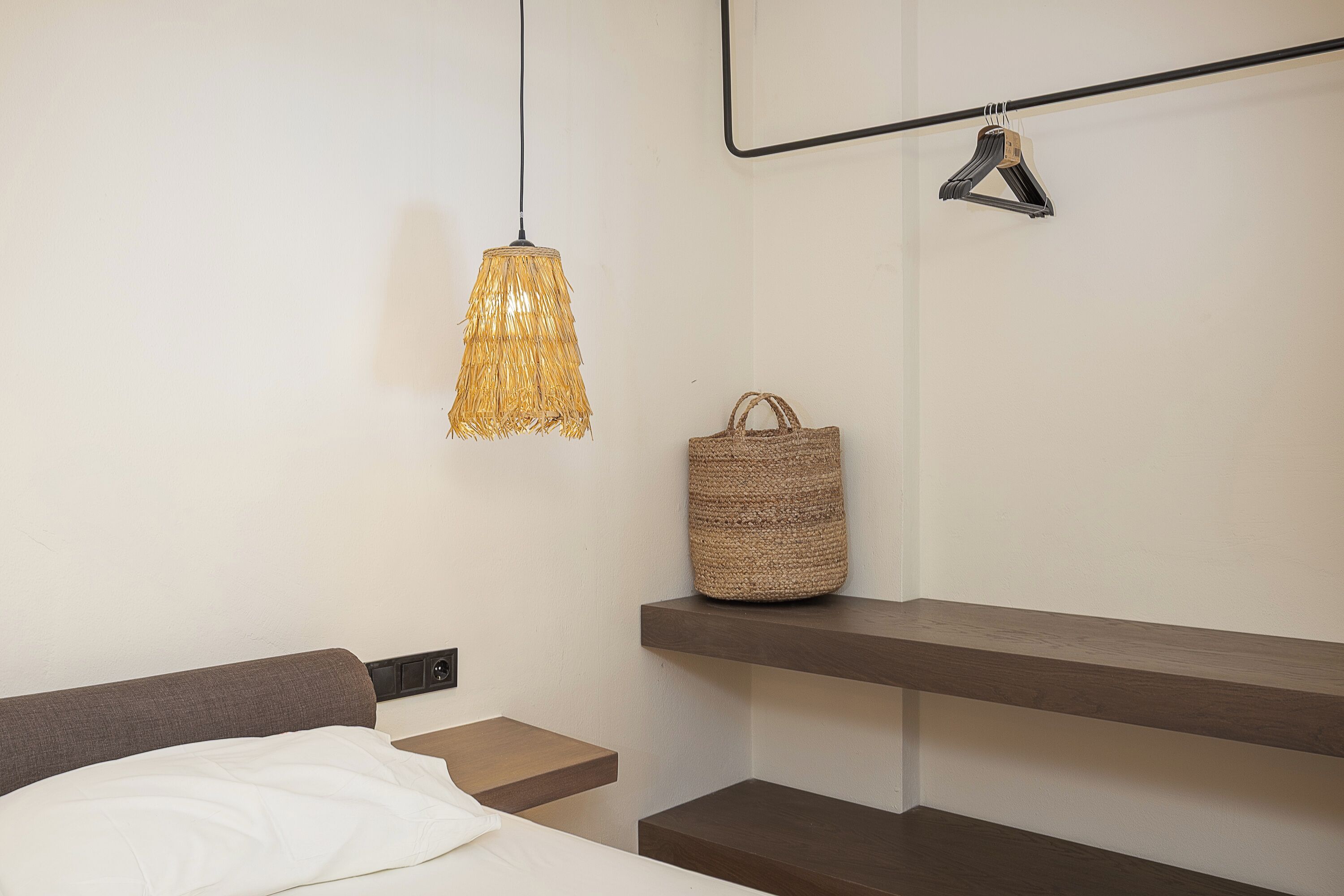 Ein Schlafzimmer mit Bett, Nachttischen, einer Hängelampe, einem Korbwägelchen und einem Regal.