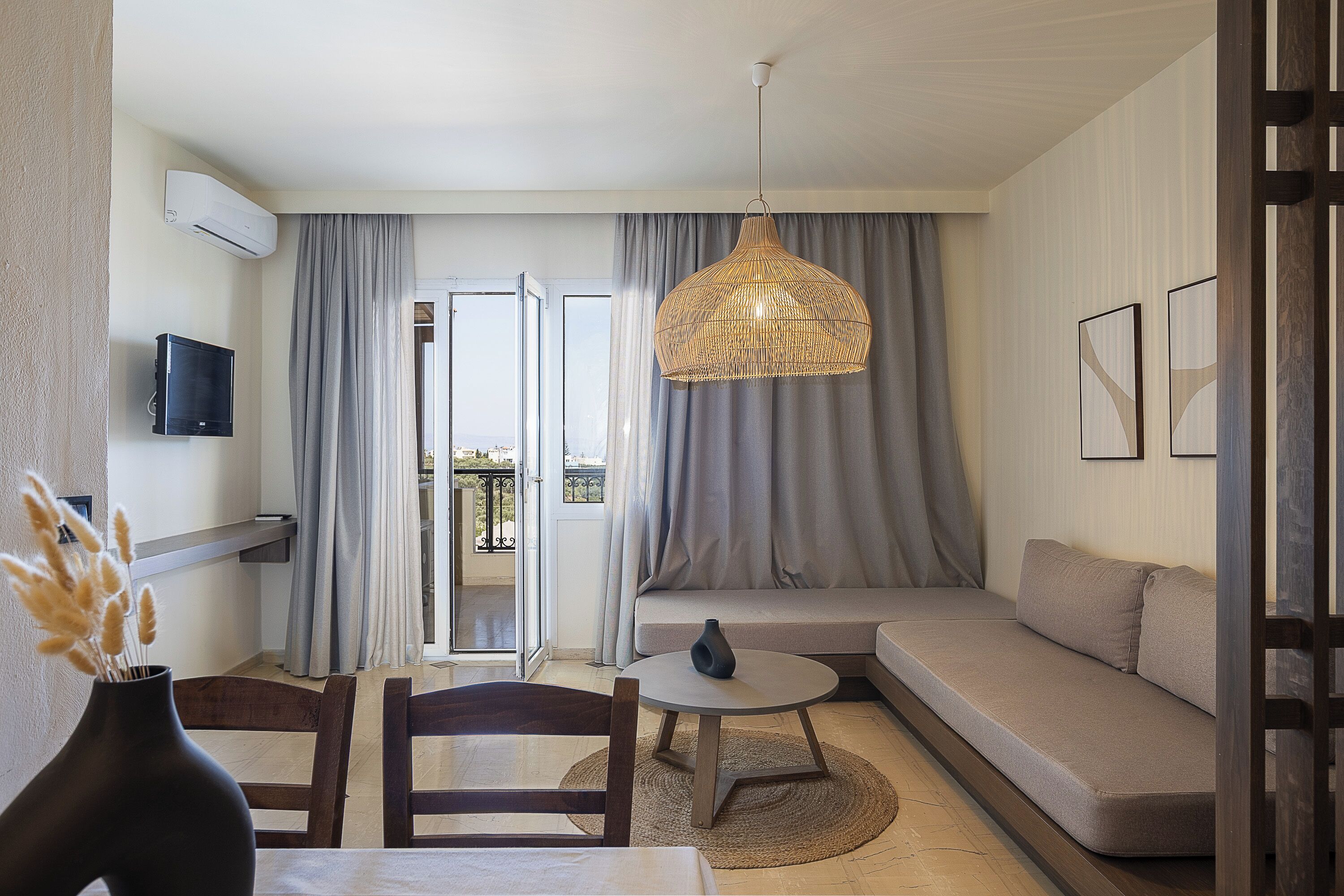 Una sala de estar moderna con un sofá, una mesa de comedor con sillas, una lámpara colgante y un televisor en la pared.