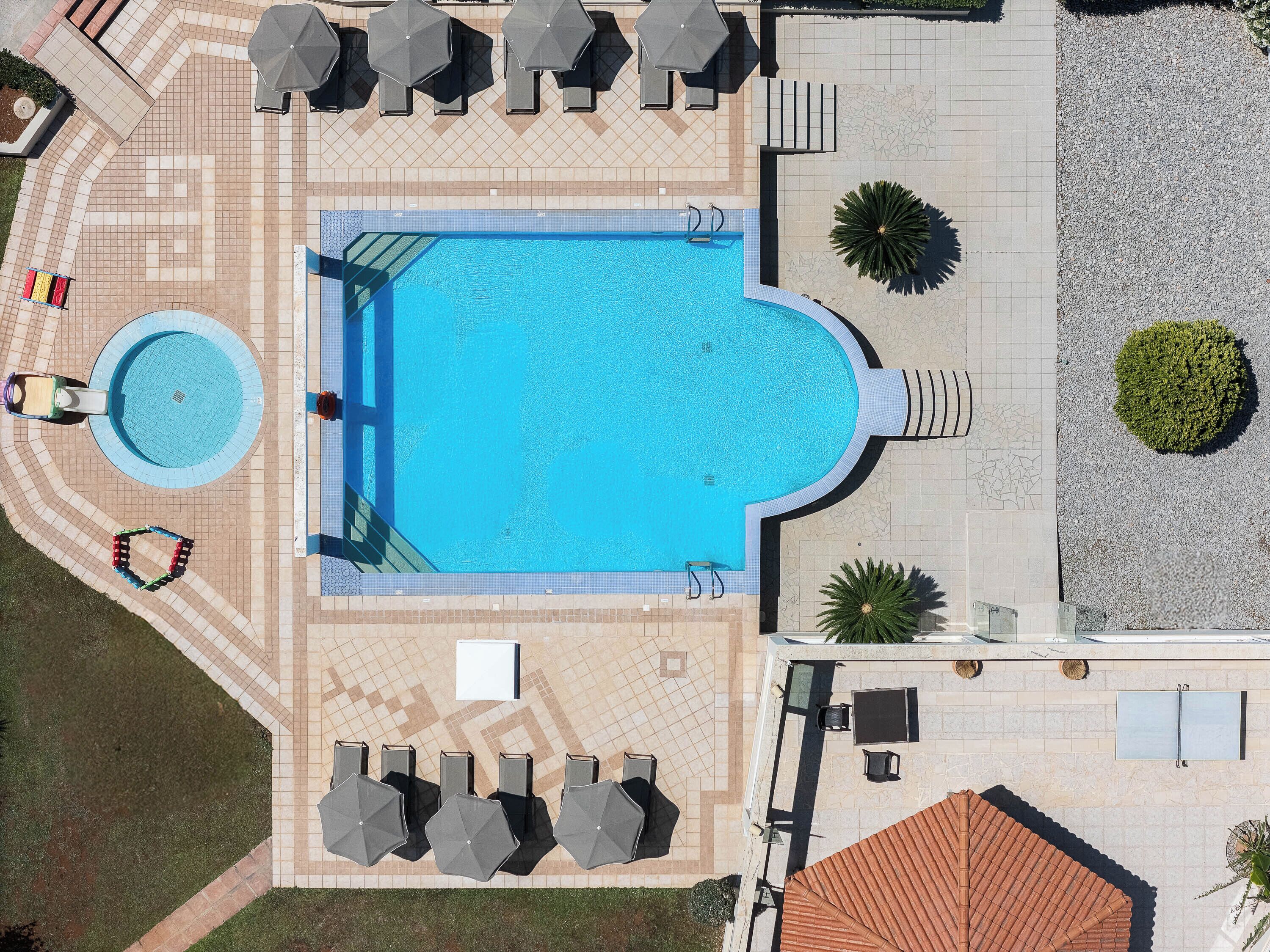 Een luchtbeeld van een zwembad met een jacuzzi, ligbedden en een overdekte zithoek.
