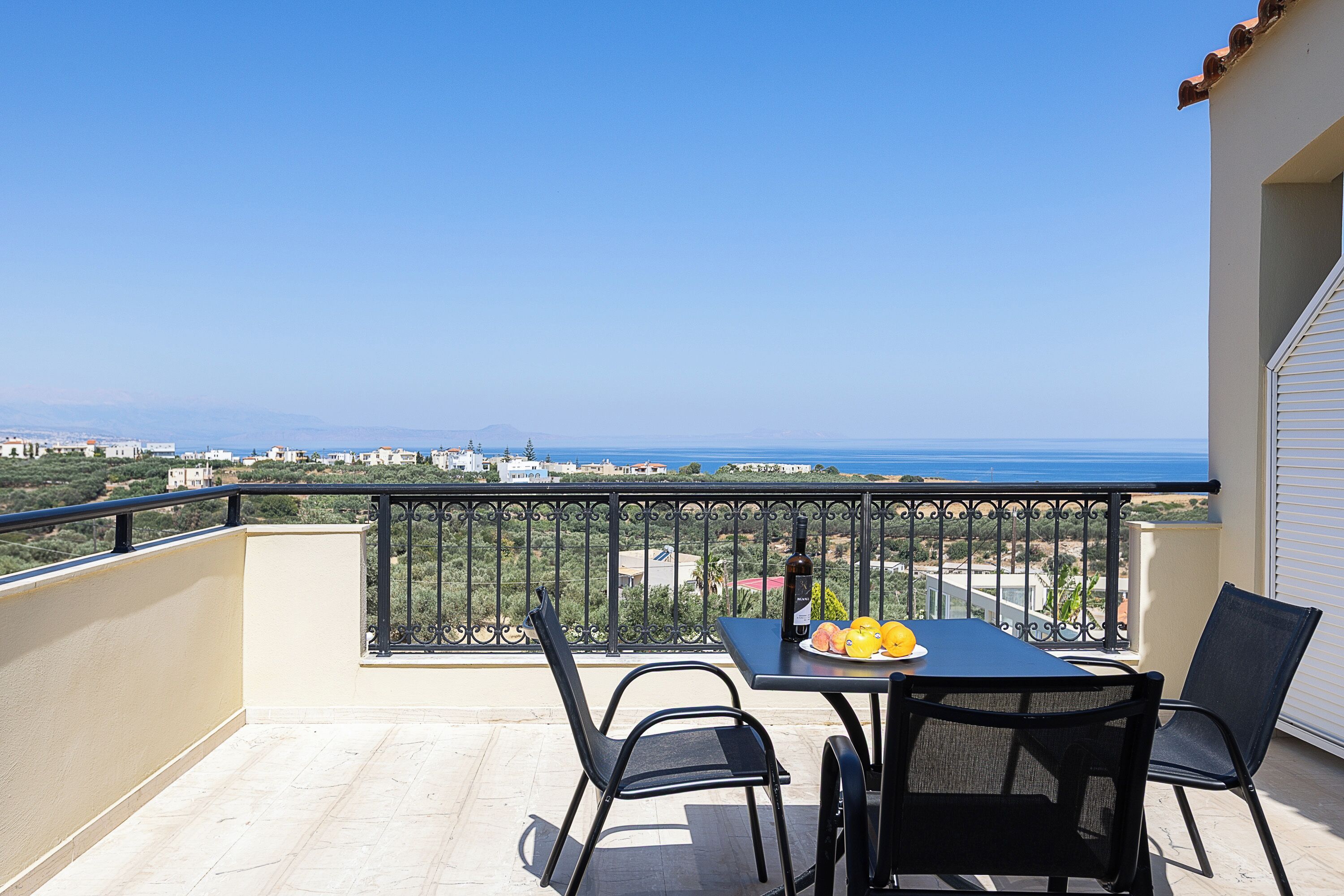 A balcony with a table, chairs, and a view of the sea.