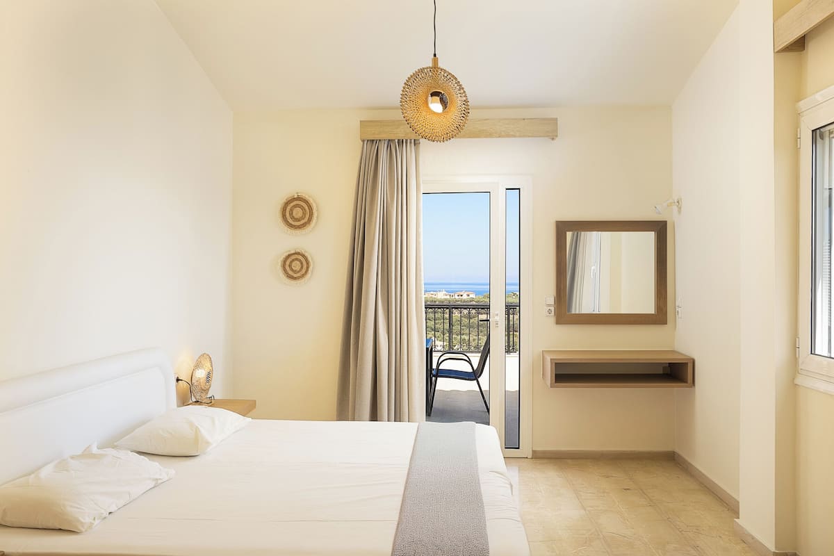 Habitación de hotel con cama, lámpara de noche, espejo, mesita y vistas al balcón exterior.