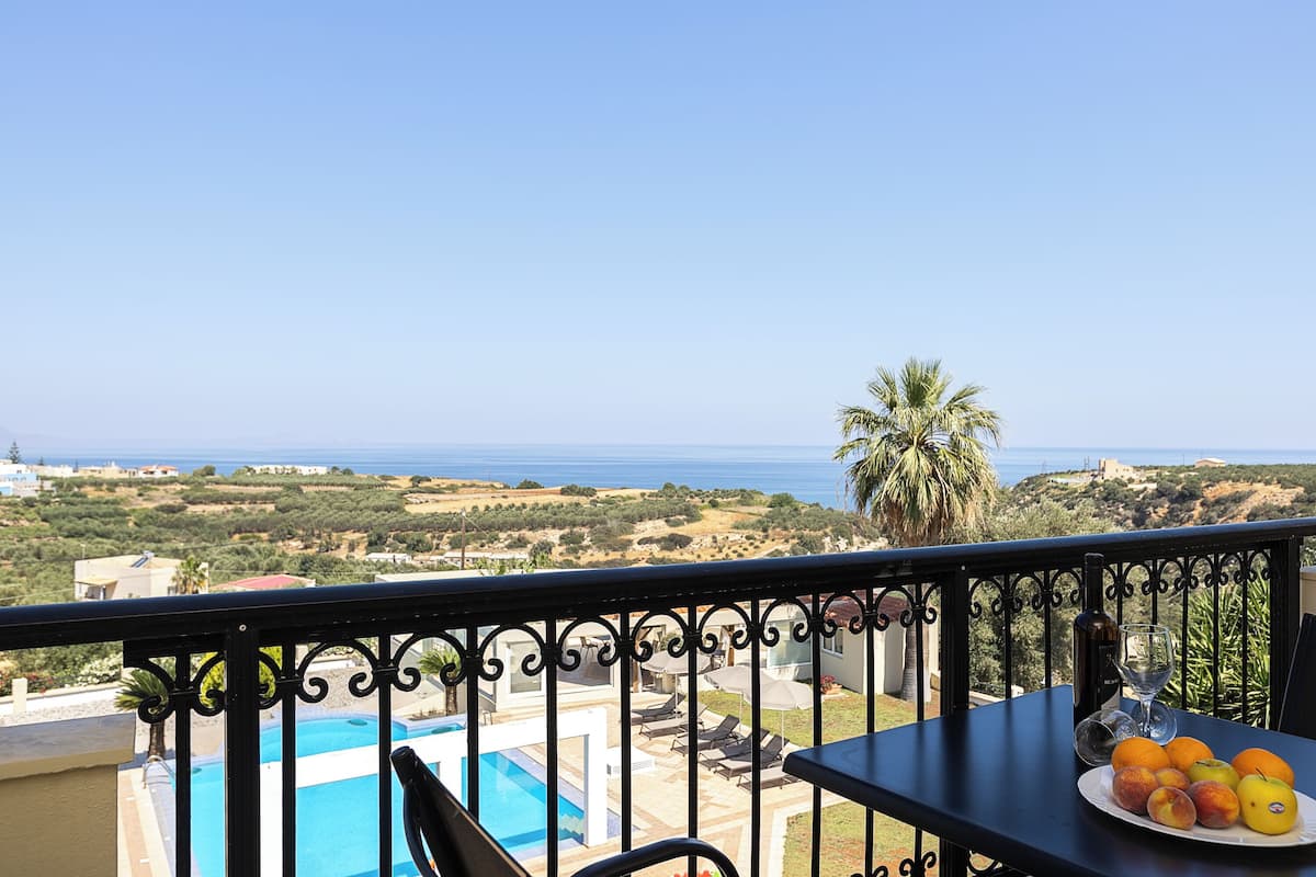 Un balcón con piscina, una mesa con fruta y vistas al mar y las colinas.