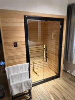 Una camera moderna con parete in legno, una porta in vetro che dà su un’area doccia e un portasciugamani con un asciugamano bianco.