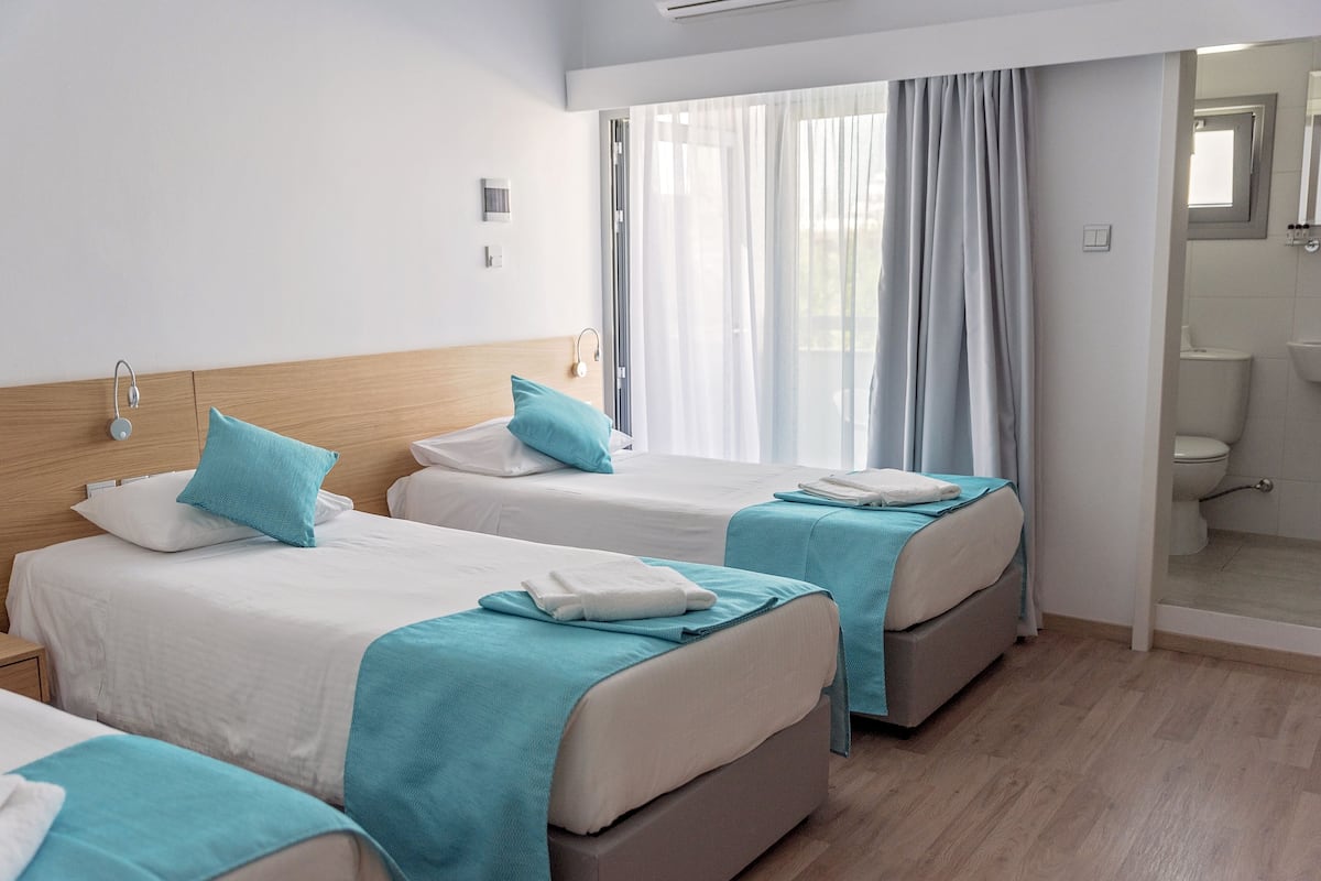 A hotel room with two beds, a bathroom, and a view of the outdoors.