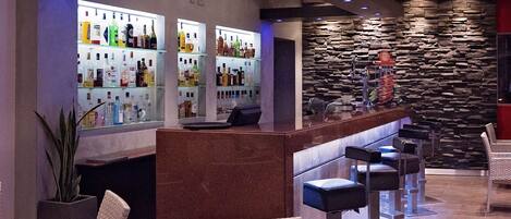 A bar area with a stone wall, multiple shelves of liquor bottles, and bar stools.