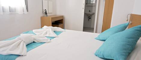 Une chambre d’hôtel avec un lit, une table de chevet en bois, une salle de bain avec un lavabo et un miroir.