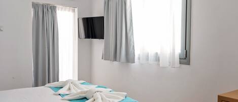 A hotel room with a bed, a TV mounted on the wall, and curtains on the windows.
