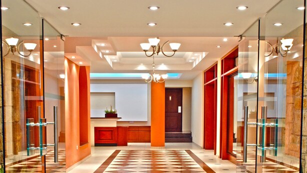 Un hall d’entrée moderne avec des portes vitrées, un sol à carreaux et un comptoir d’accueil central.