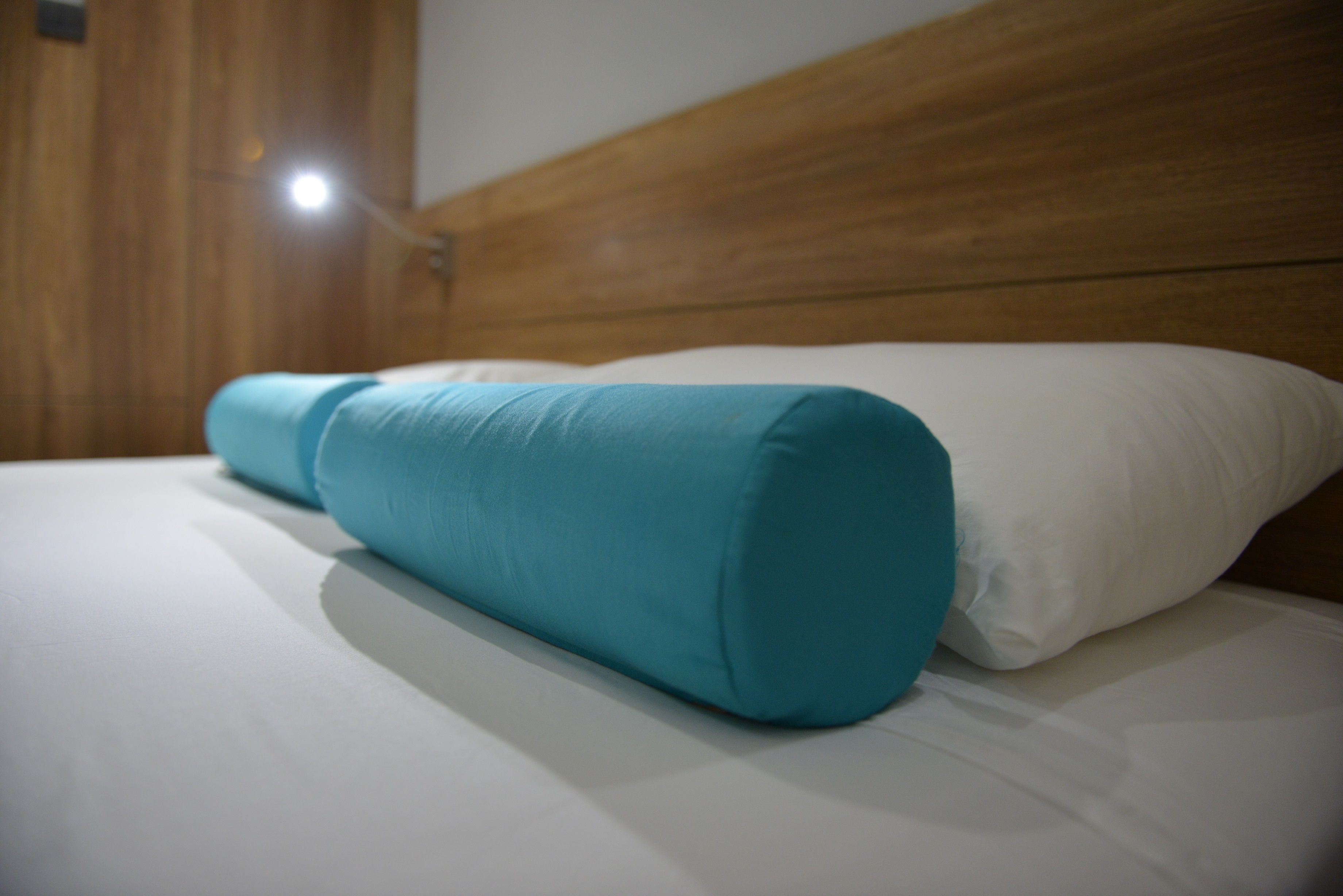Ein Bett mit einem hölzernen Kopfteil und einem türkisfarbenen Kopfkissen.