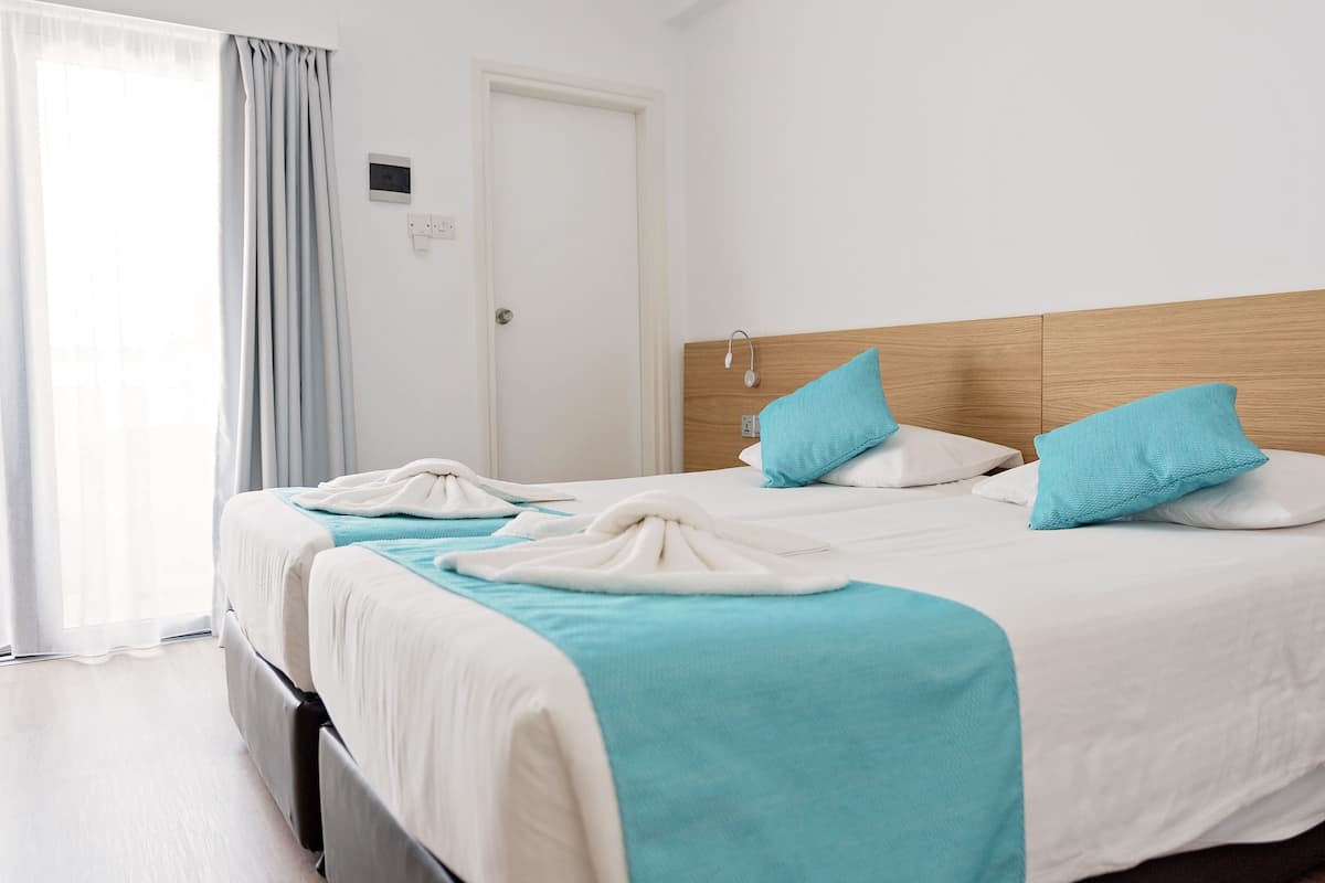 A hotel room with a bed, a door, and a window with curtains.
