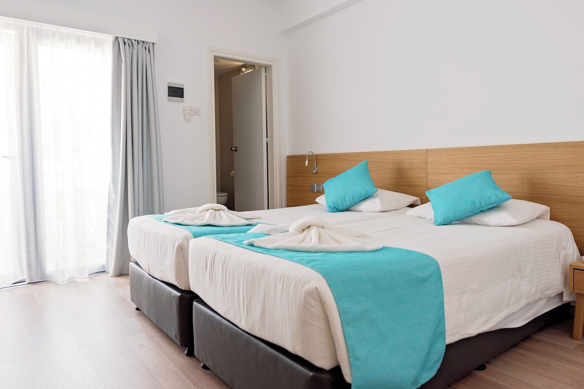 A hotel room with two beds, a wooden headboard, and a view of the bathroom through an open door.