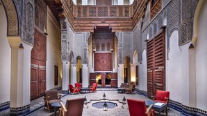 A courtyard with a central fountain, red and brown chairs, and intricate tile work on the walls and floor. - Dar Bensouda (Fes)
