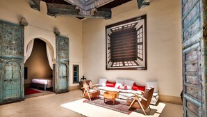 A room with a high ceiling, a skylight, a large bed with red and white bedding, a sofa with red cushions, and a wooden coffee table. - Dar Bensouda (Fes)