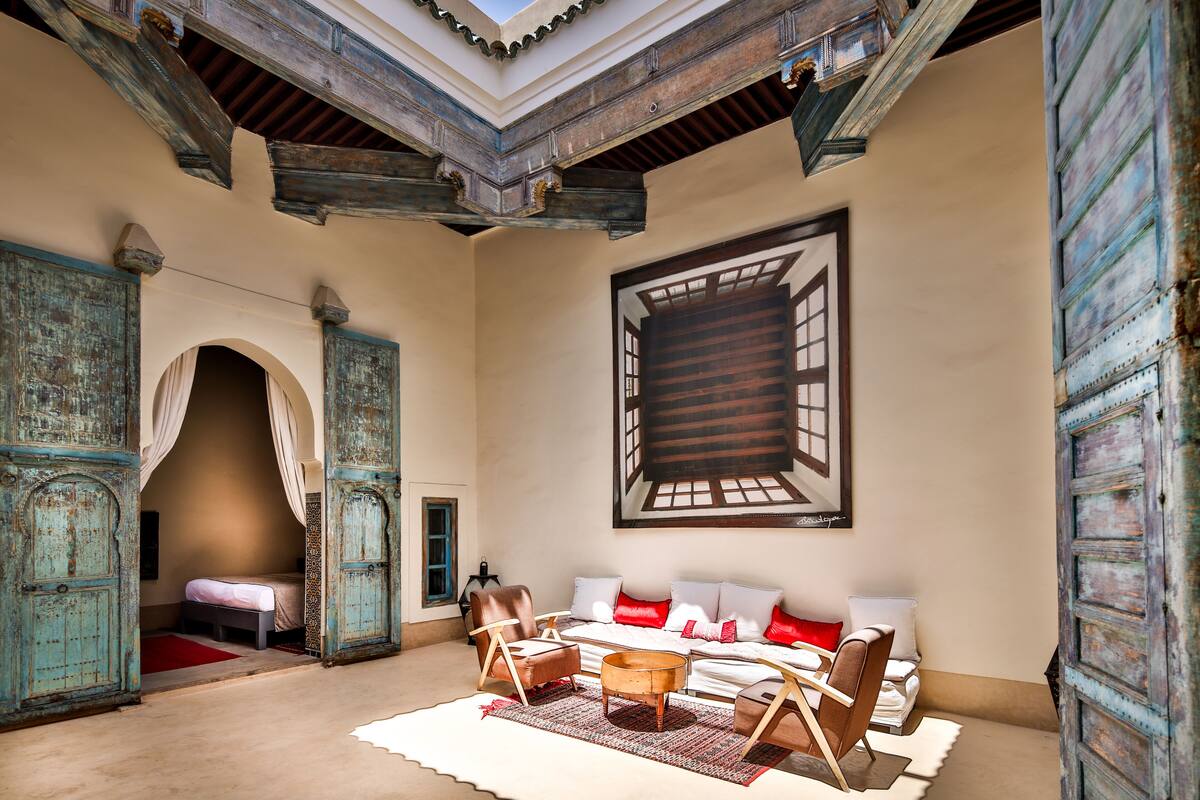 A room with a high ceiling, a skylight, a large bed with red and white bedding, a sofa with red cushions, and a wooden coffee table.