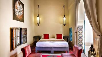 Una habitación de hotel con una cama grande, dos sillas rojas, una mesita pequeña y un farol decorativo.
